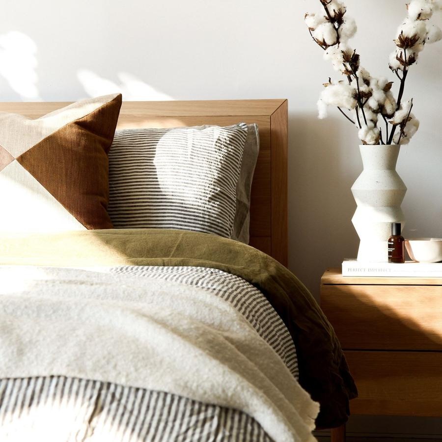 swath of sunlight shines across a well made bed and bedside table with a vase of cotton plants
